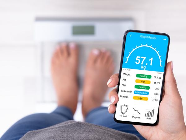 A woman standing on a bathroom scale, reading her weight and body fat on a phone app